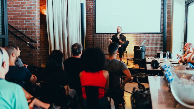 man-sitting-on-chair-while-giving-conference-to-big-group-of-people-communication-coach